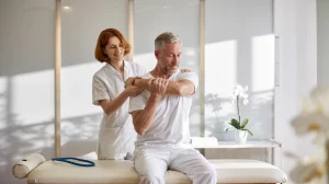 Fisioterapeuta asistiendo a un paciente senior en ejercicios de movilidad de hombro para mejorar la calidad de vida en Clínica Trajano.